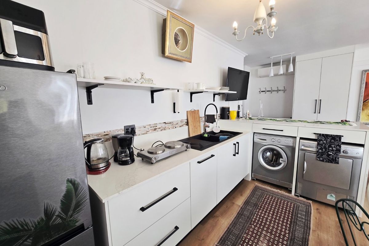 A compact kitchen featuring white cabinetry, stone countertops, a black sink, and integrated laundry appliances, finished with a decorative chandelier.