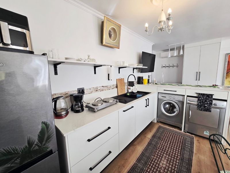 A compact kitchen featuring white cabinetry, stone countertops, a black sink, and integrated laundry appliances, finished with a decorative chandelier.