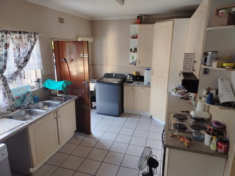 A functional kitchen featuring tiled flooring, laminate countertops, built-in cabinetry, and an electric hob, offering a practical layout for daily use.