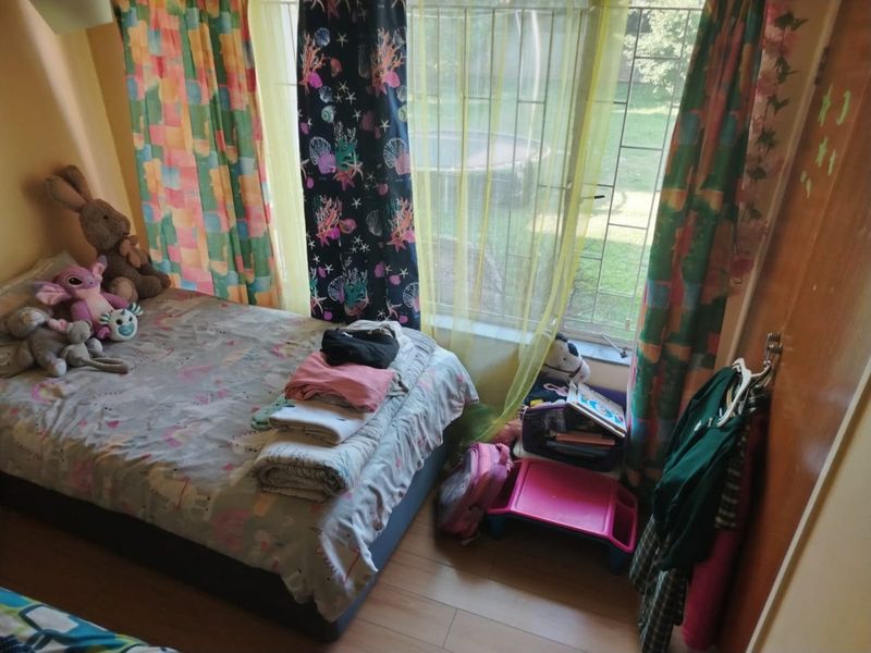 A bedroom featuring laminate flooring and a window fitted with security bars, overlooking the garden area.