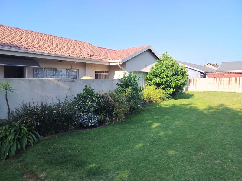 A view of the rear garden featuring a well-maintained lawn, established garden beds, and the rear elevation of the house with a tiled roof.