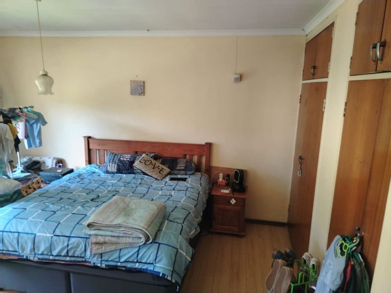 A functional bedroom featuring laminate flooring, built-in wooden cupboards, and a simple pendant light fixture, offering a neutral base for potential updates.