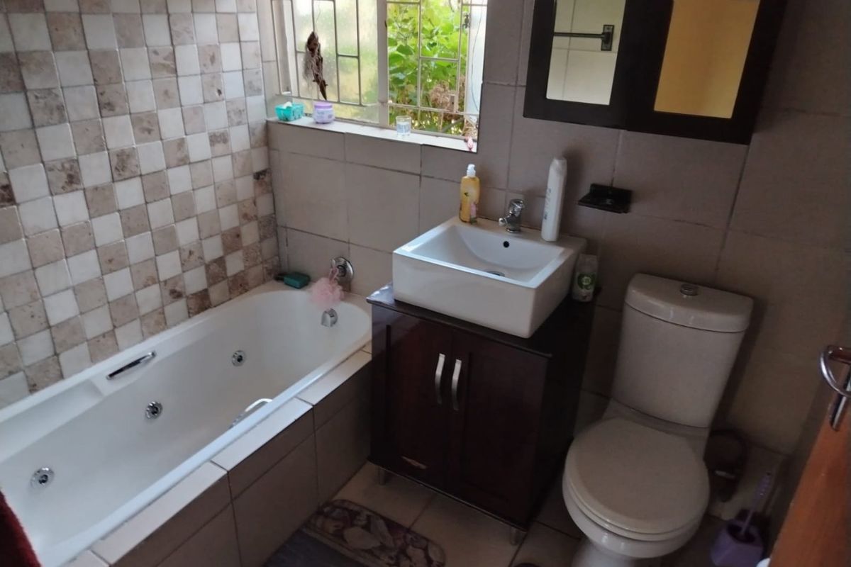 A functional bathroom featuring a built-in bathtub, a modern vessel sink with vanity cabinet, and a standard toilet with tiled finishes.