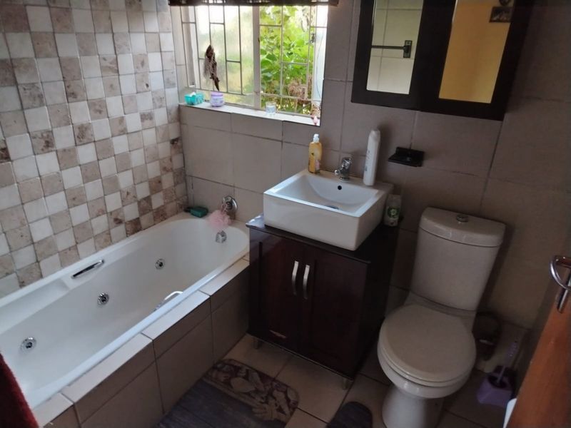 A functional bathroom featuring a built-in bathtub, a modern vessel sink with vanity cabinet, and a standard toilet with tiled finishes.