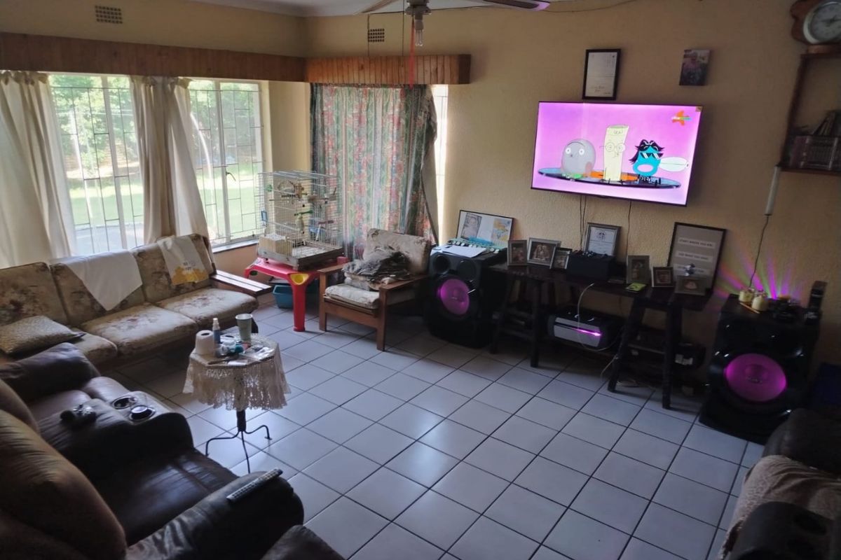 A spacious living room featuring tiled flooring, a ceiling fan, and large windows with timber pelmets, offering a functional and well-lit living area.