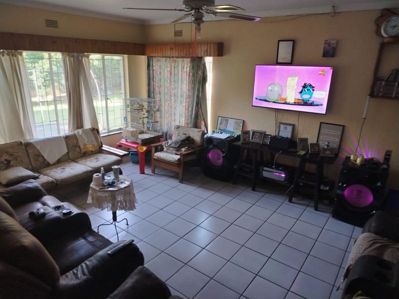 A spacious living room featuring tiled flooring, a ceiling fan, and large windows with timber pelmets, offering a functional and well-lit living area.