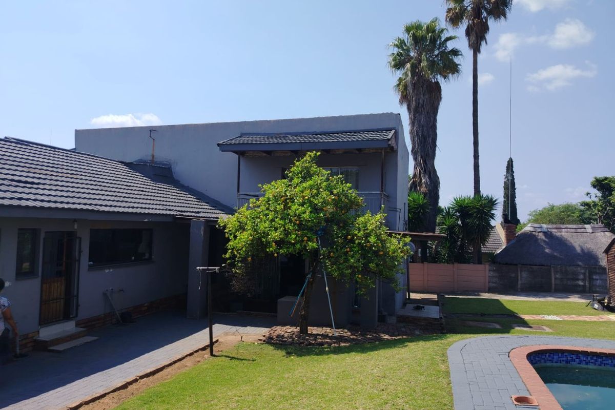 Rear view of the property featuring a tiled roof, balcony, paved patio area, and a swimming pool set within a landscaped garden.