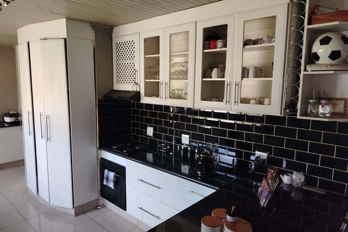 A functional kitchen featuring white cabinetry, black subway tile backsplash, dark granite countertops, and integrated appliances with glass-fronted display units.