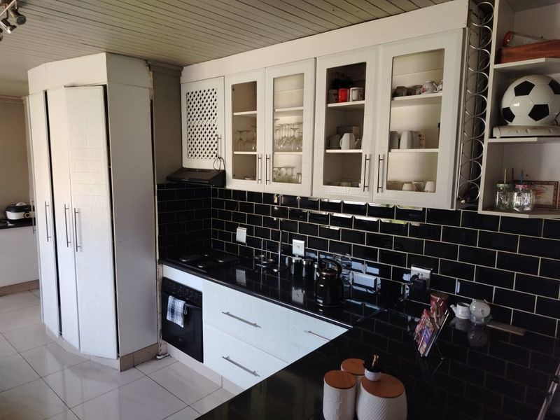 A functional kitchen featuring white cabinetry, black subway tile backsplash, dark granite countertops, and integrated appliances with glass-fronted display units.