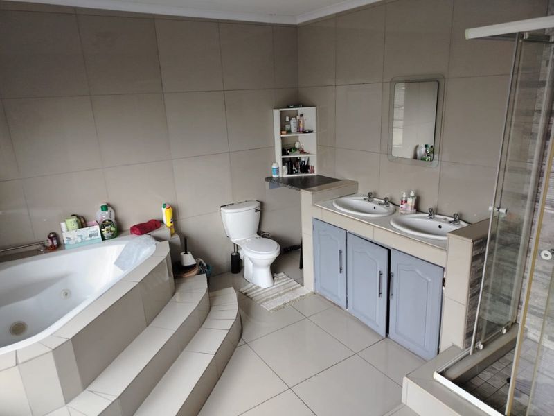 Spacious bathroom featuring a built-in corner bathtub, double vanity with storage, toilet, and a separate shower enclosure with neutral wall and floor tiling.