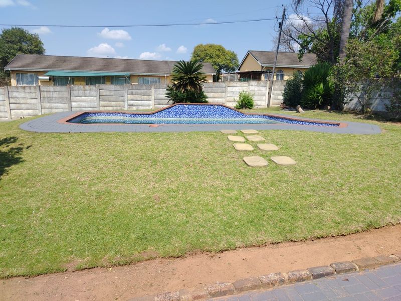 A backyard swimming pool area featuring a raised tiled pool edge, surrounding lawn, and a precast concrete boundary wall.
