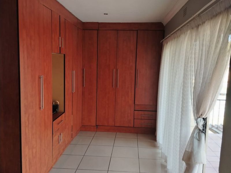 A bright bedroom featuring extensive built-in wooden cupboards, neutral tiled flooring, and a sliding glass door providing access to an outdoor area.