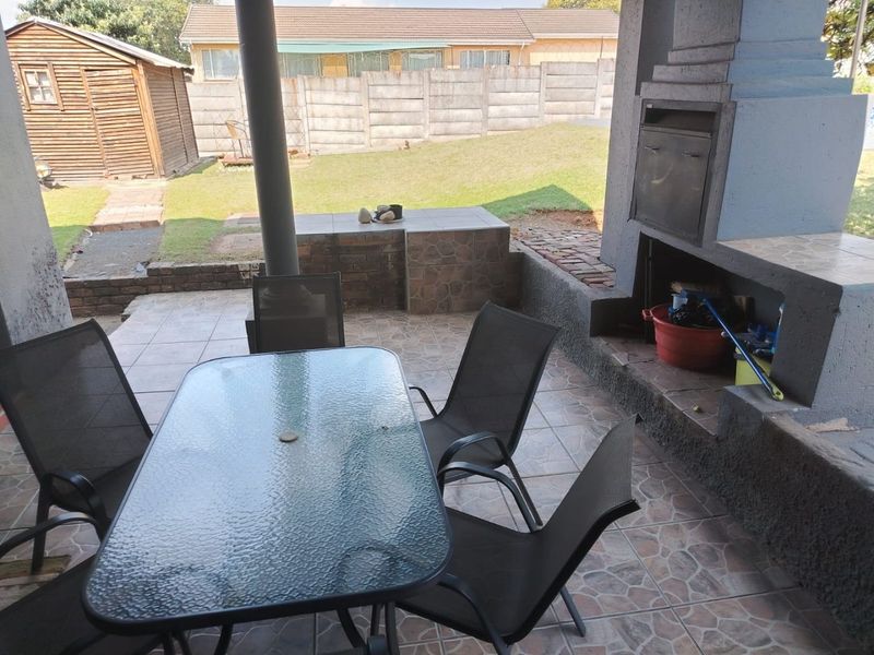 Covered patio area featuring a built-in braai, tiled flooring, and direct access to the rear garden and yard space.