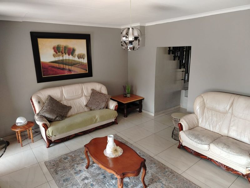A living room featuring neutral grey walls, tiled flooring, and a modern pendant light fixture, providing a functional and well-maintained space.
