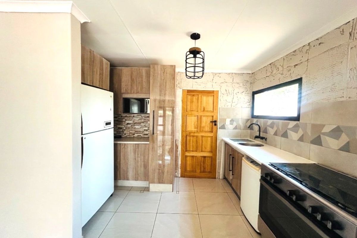 A functional kitchen featuring wood-look cabinetry, stone countertops, tiled backsplash, and a freestanding stove, with direct access to an exterior door.