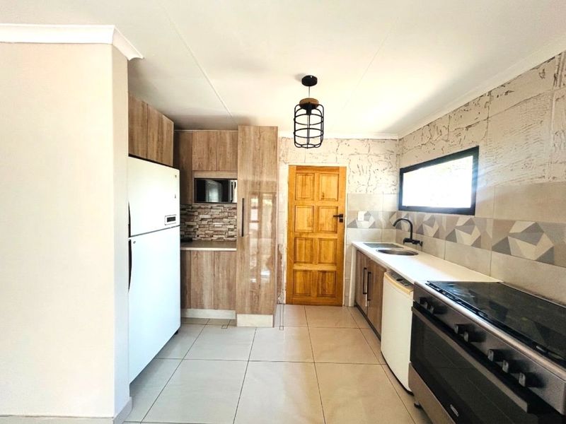 A functional kitchen featuring wood-look cabinetry, stone countertops, tiled backsplash, and a freestanding stove, with direct access to an exterior door.