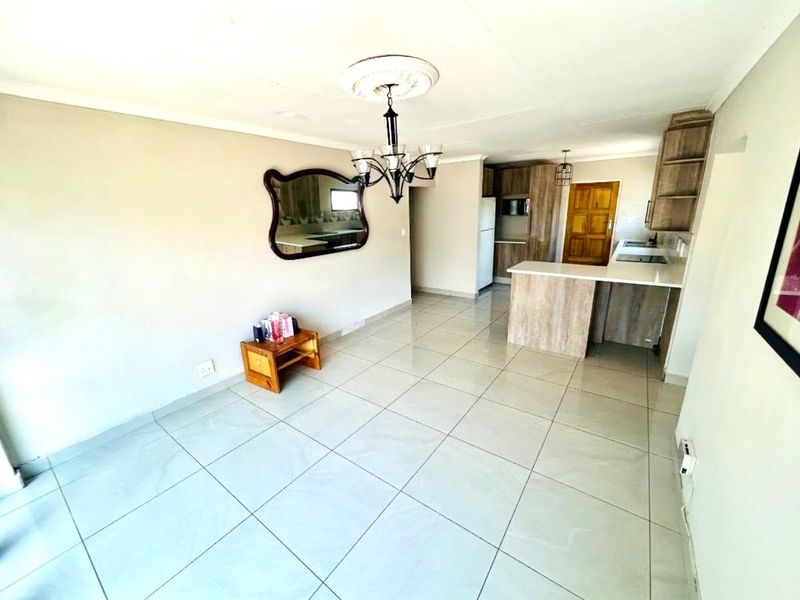 An open-plan living and kitchen area featuring modern tiled flooring, neutral walls, and a functional kitchen with stone countertops and built-in cabinetry.