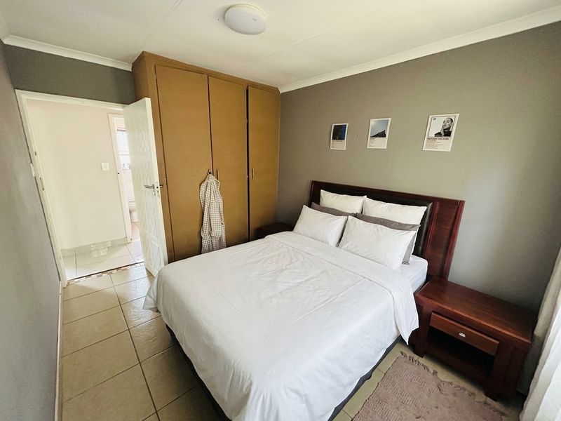 A functional bedroom featuring built-in cupboards, tiled flooring, and neutral wall tones, offering a clean and practical living space.