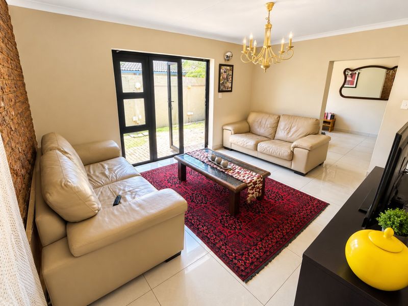 A bright living room featuring polished tile floors, an exposed brick feature wall, and double glass doors leading to the outdoor area.