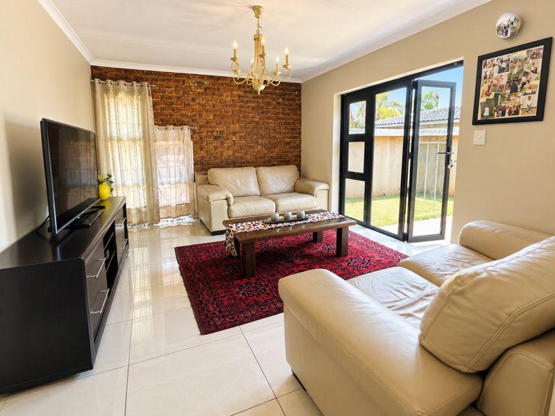 Bright living room featuring an exposed brick accent wall, polished tile flooring, and black aluminium bifold doors providing direct access to the garden.