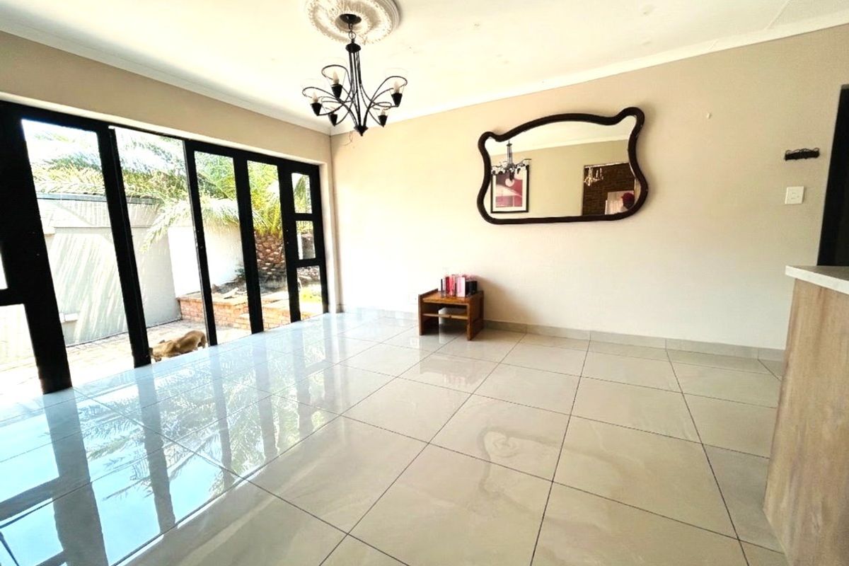 Spacious living area featuring large black-framed sliding glass doors, polished floor tiles, and a decorative ceiling rose with a chandelier.