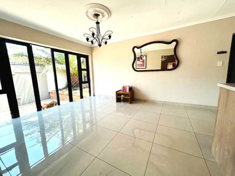 Spacious living area featuring large black-framed sliding glass doors, polished floor tiles, and a decorative ceiling rose with a chandelier.
