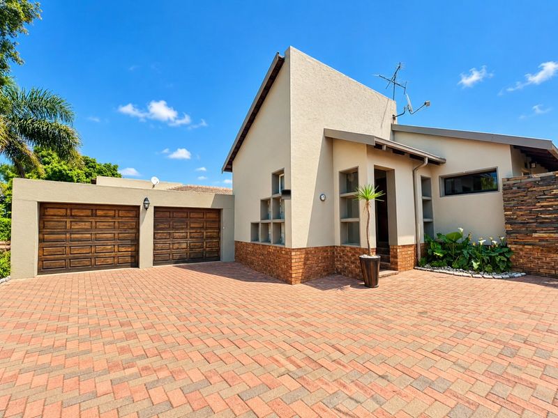 Front elevation of a modern townhouse featuring a double garage, paved driveway, and attractive combination of brick and stone exterior finishes.