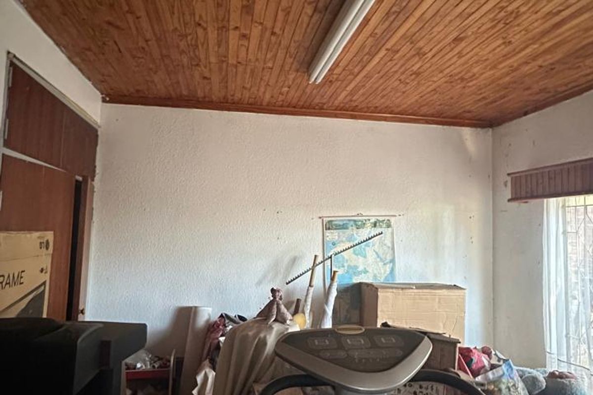 A bedroom featuring a timber tongue and groove ceiling and built-in storage, currently used for storage and in need of renovation.