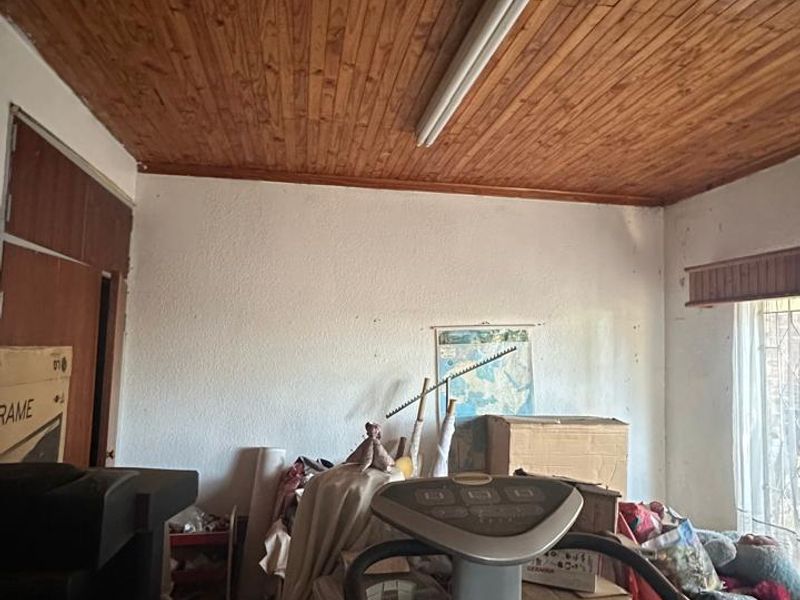 A bedroom featuring a timber tongue and groove ceiling and built-in storage, currently used for storage and in need of renovation.