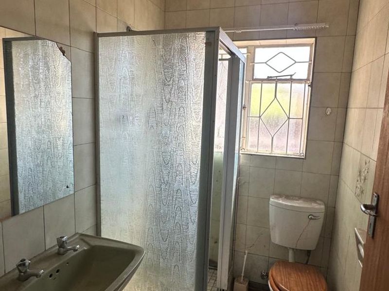 A dated bathroom featuring a shower cubicle, pedestal basin, and toilet, requiring renovation to update the finishes and fixtures.
