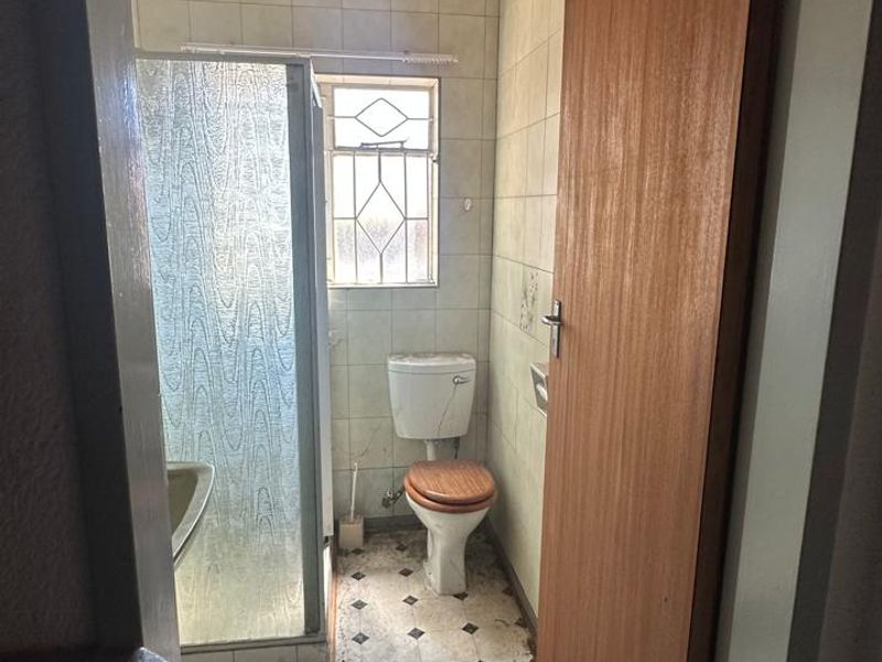 A dated bathroom featuring a shower enclosure, toilet, and tiled walls. The space requires renovation to update the finishes and flooring.
