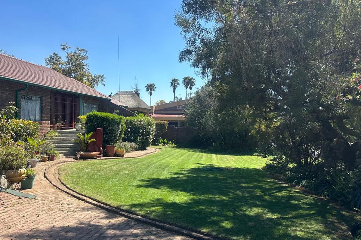 A well-maintained rear garden featuring a manicured lawn, brick paved pathway, and a brick-built house with a tiled roof and security entrance.