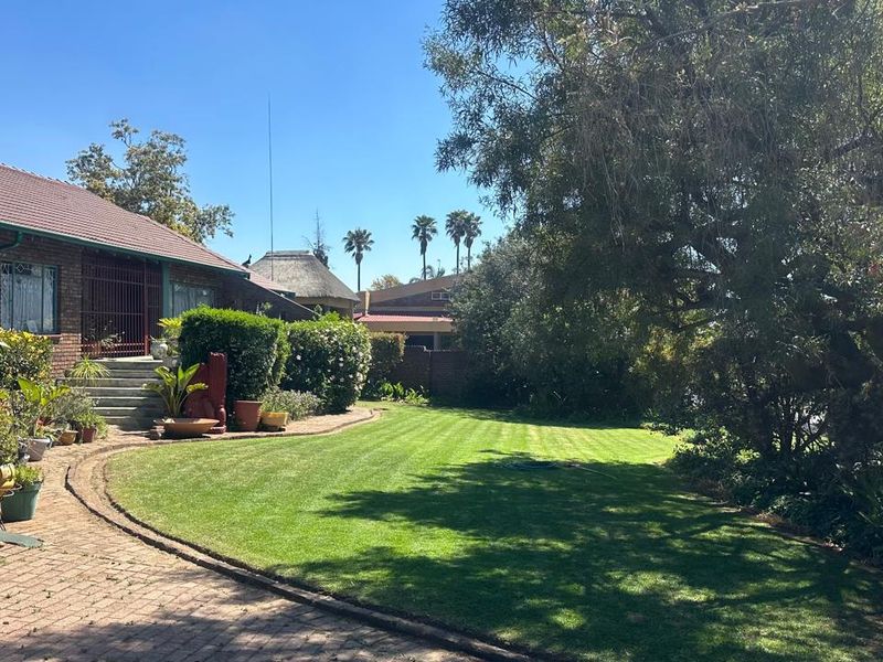 A well-maintained rear garden featuring a manicured lawn, brick paved pathway, and a brick-built house with a tiled roof and security entrance.