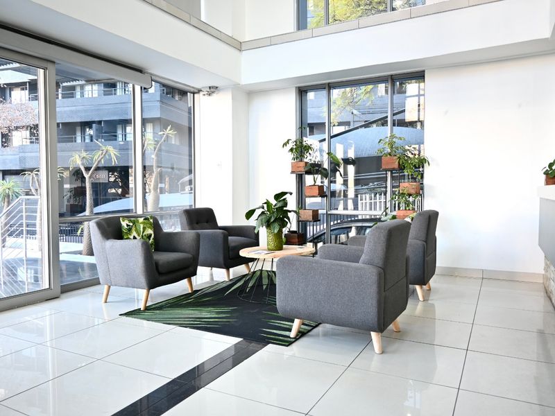 Bright and modern commercial entrance lobby featuring double volume ceilings, large floor-to-ceiling windows, and polished tile flooring.