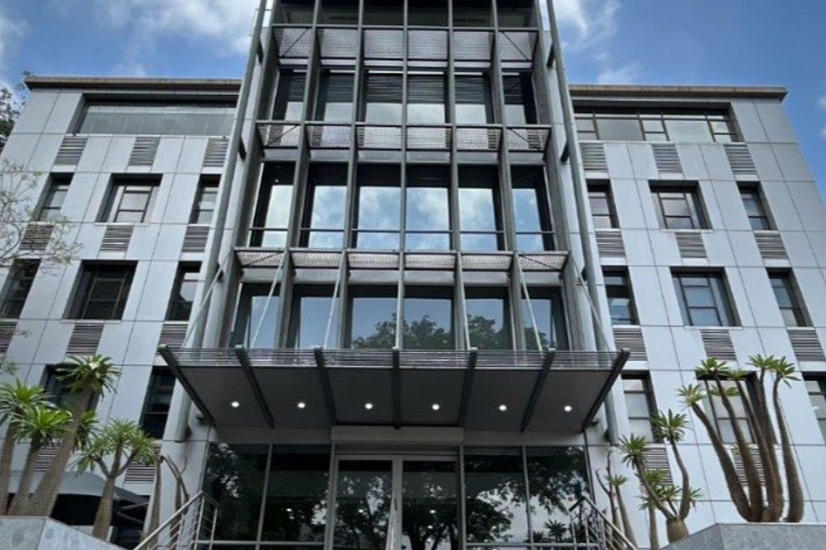 Modern commercial office building facade featuring a glass curtain wall, metal cladding, and a prominent entrance canopy with integrated lighting.
