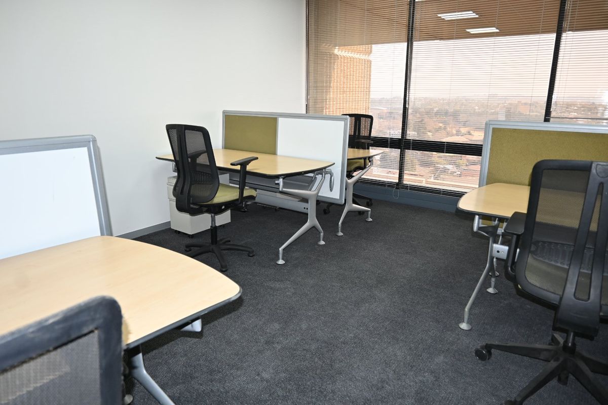 A functional commercial office space featuring carpeted flooring, large windows with venetian blinds, and built-in desk partitions for a professional work environment.