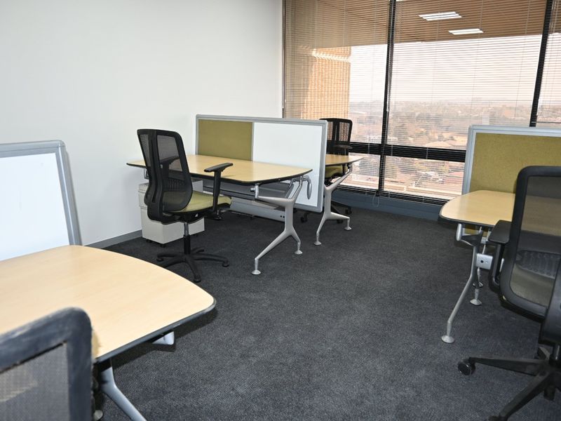 A functional commercial office space featuring carpeted flooring, large windows with venetian blinds, and built-in desk partitions for a professional work environment.