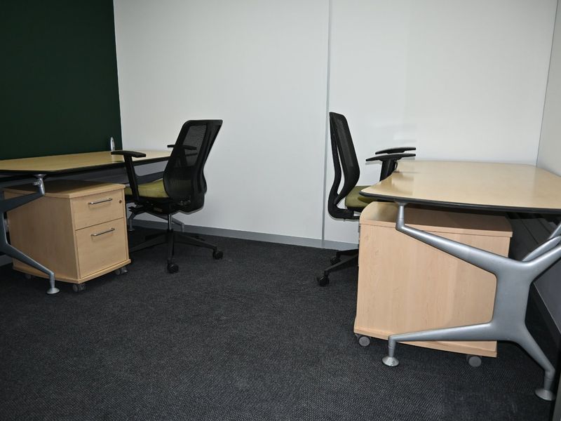 A functional office space featuring dark carpet flooring and a contrasting green accent wall, suitable for a professional work environment.