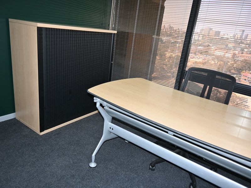 A professional office space featuring large windows with venetian blinds, offering an expansive city view and carpeted flooring.