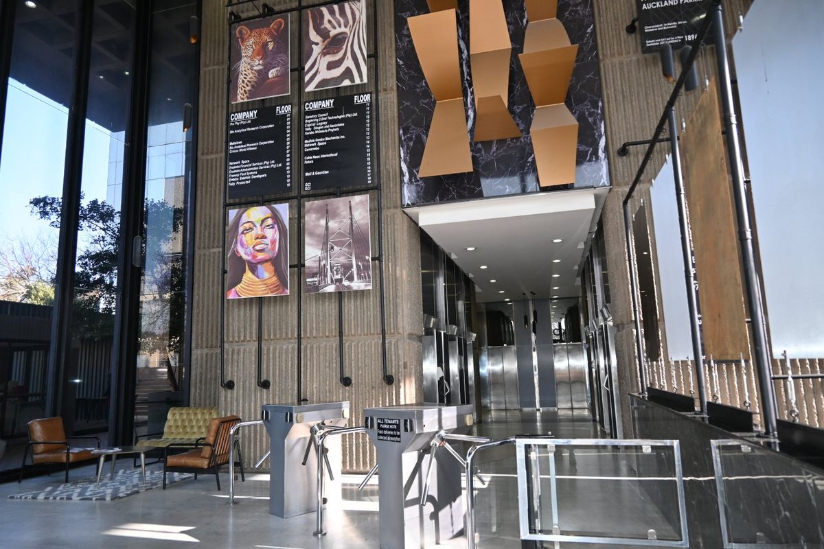 Modern commercial building lobby featuring high ceilings, textured concrete and marble finishes, security turnstiles, and stainless steel elevator access.