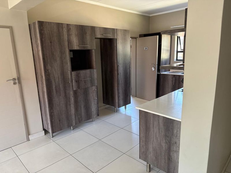 A modern kitchen area featuring dark wood-grain cabinetry, light countertops, and neutral tiled flooring, presenting a clean and functional space.
