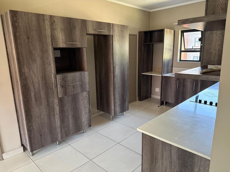 Modern kitchen featuring dark wood-look cabinetry, light countertops, tiled flooring, and a built-in hob, offering a clean and functional workspace.