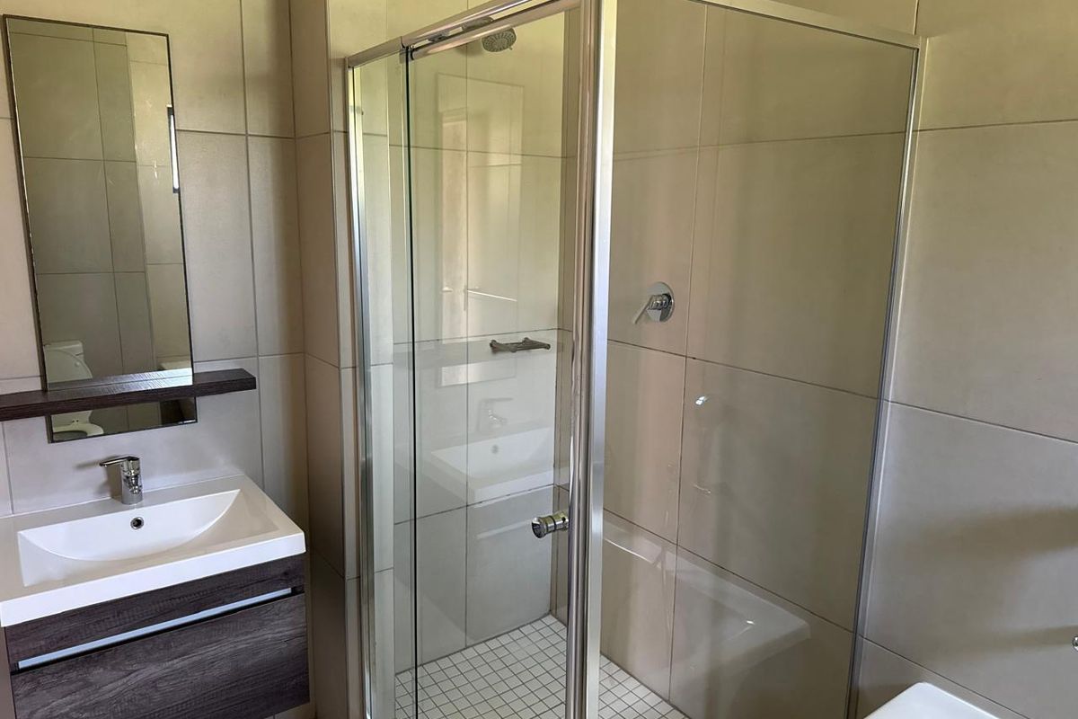 A modern bathroom featuring a glass-enclosed shower, a vanity cabinet with a basin, and neutral wall tiling.