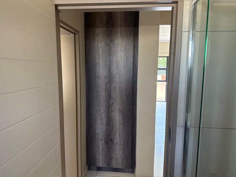 A clean hallway featuring a modern dark wood-grain built-in cupboard and tiled flooring, providing a functional transition space within the townhouse.