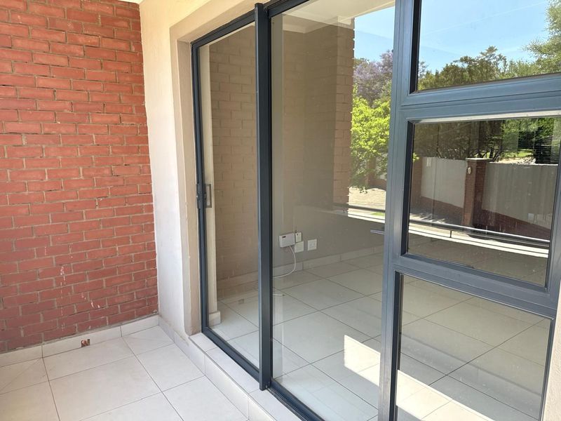 A covered patio area featuring exposed brickwork, tiled flooring, and large sliding glass doors providing access to the interior living space.