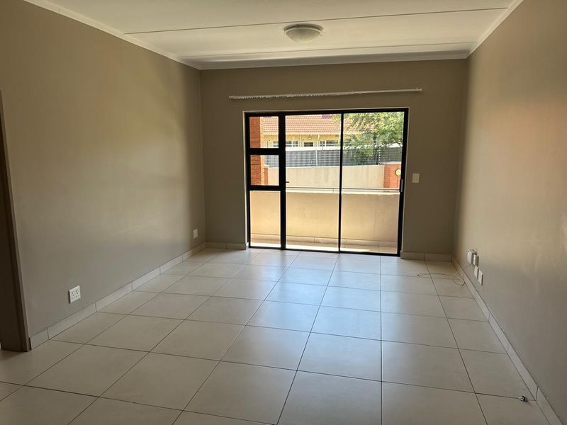 A bright, empty living room featuring neutral tiled flooring and a large sliding glass door providing access to an outdoor balcony area.