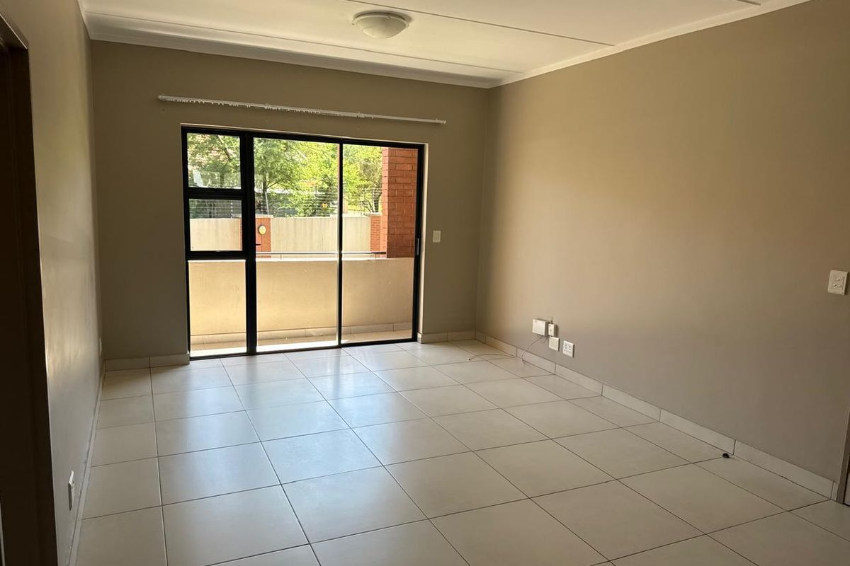 A bright, empty living room featuring neutral tiled flooring and a large sliding glass door that provides access to an outdoor balcony area.