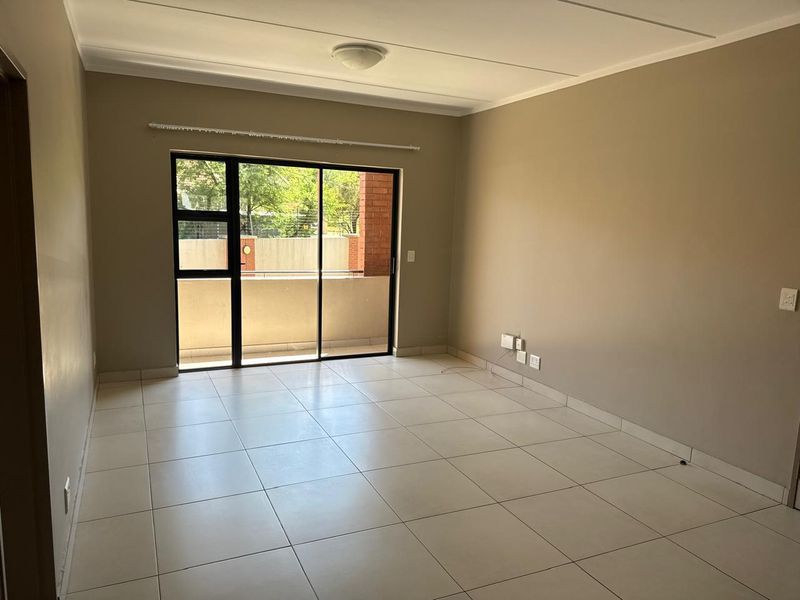 A bright, empty living room featuring neutral tiled flooring and a large sliding glass door that provides access to an outdoor balcony area.