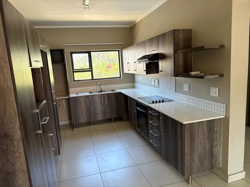 A modern, empty kitchen featuring dark wood-look cabinetry, stone countertops, a built-in oven, electric hob, and a tiled backsplash with a window view.