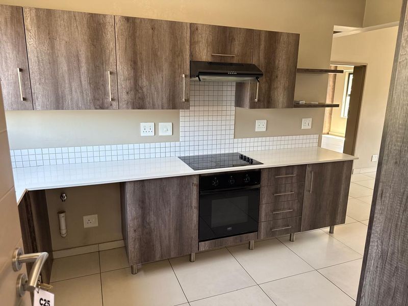 Modern kitchen featuring wood-look cabinetry, white quartz countertops, a tiled backsplash, and integrated appliances including an electric hob and oven.